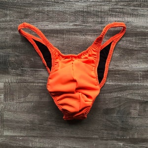 Puede incluir: Bañador naranja con ribetes negros. El bañador tiene la espalda baja y la pierna alta.