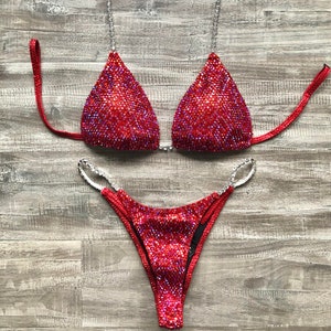 May include: Red sparkly bikini with silver embellishments. The top is a triangle style with adjustable straps. The bottom is a cheeky style with a high cut leg.