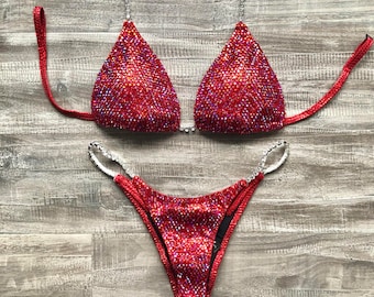 May include: Red sparkly bikini with silver embellishments. The top is a triangle style with adjustable straps. The bottom is a cheeky style with a high cut leg.