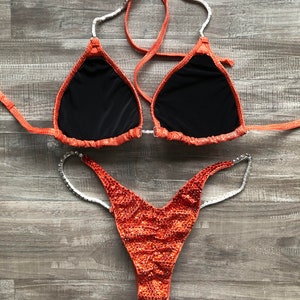 Puede incluir: Parte superior e inferior de bikini de lentejuelas naranja y plata. La parte superior tiene forma de tri&aacute;ngulo y la parte inferior es de estilo de corte alto.