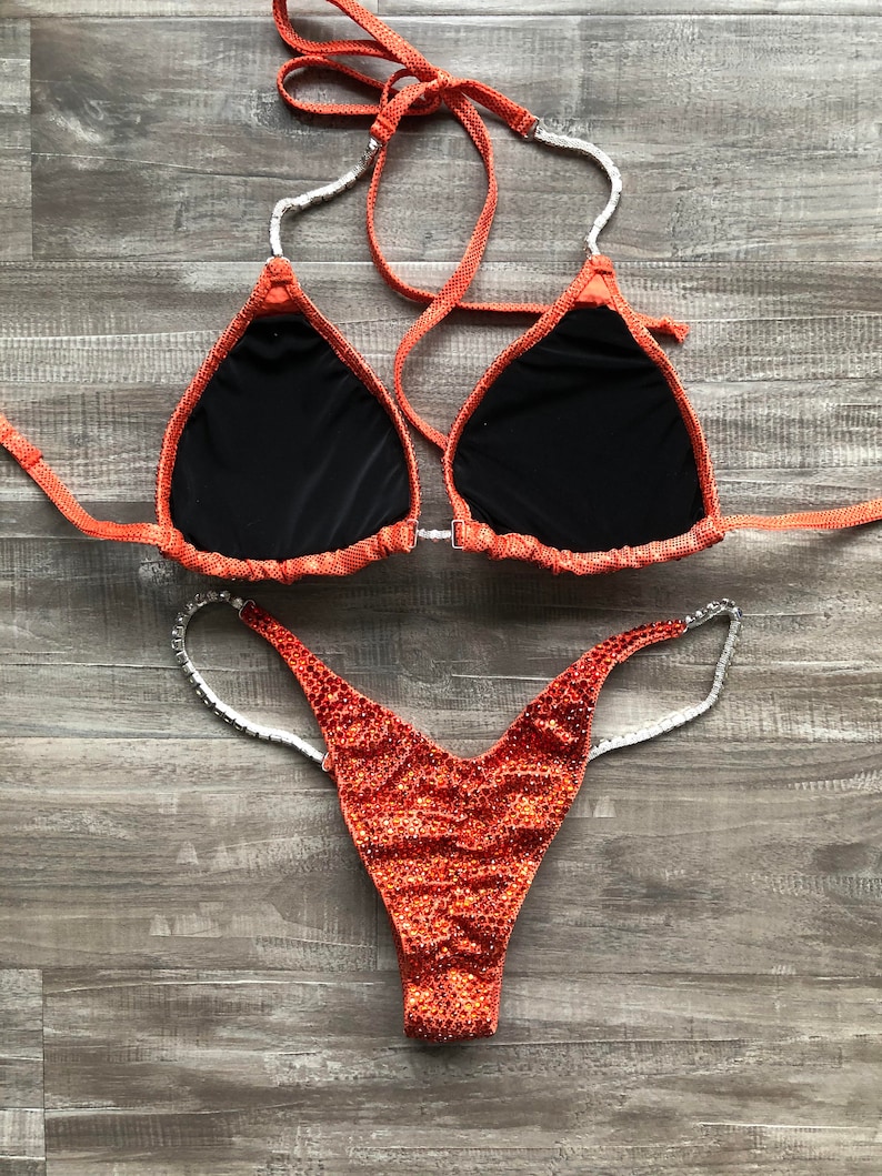 Puede incluir: Parte superior e inferior de bikini de lentejuelas naranja y plata. La parte superior tiene forma de tri&aacute;ngulo y la parte inferior es de estilo de corte alto.