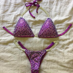 Pu&ograve; includere: Bikini con paillettes viola e argento con un top halter e uno slip a vita alta.