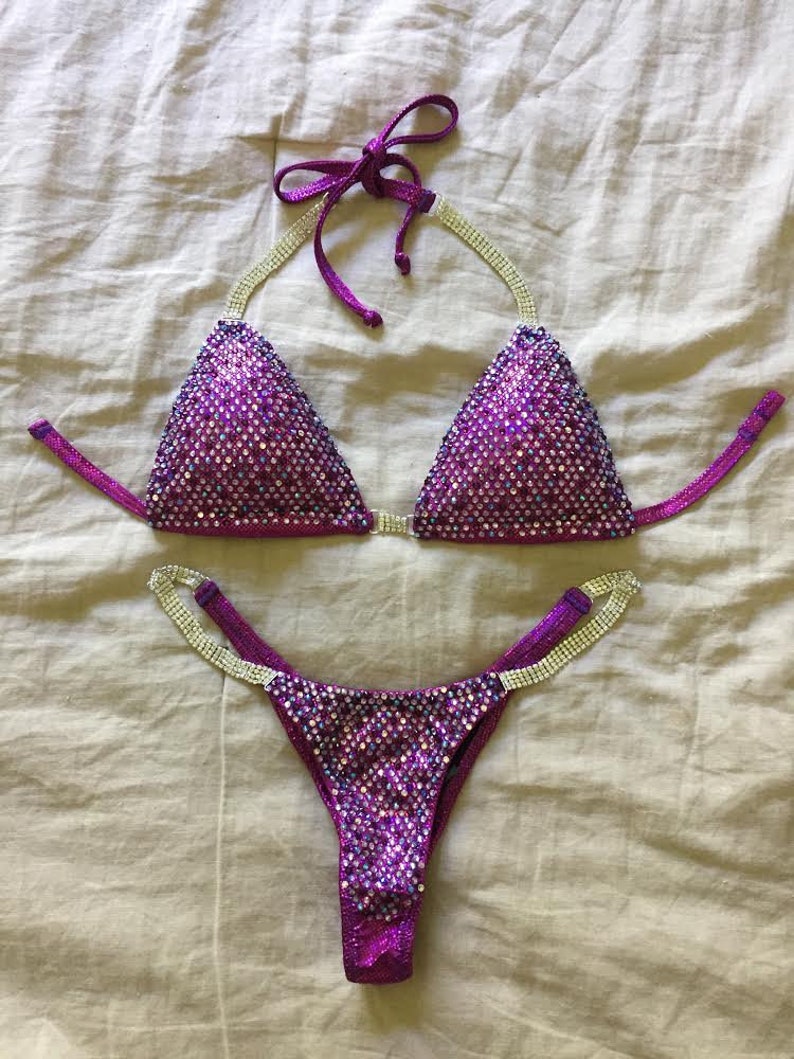 Pu&ograve; includere: Bikini con paillettes viola e argento con un top halter e uno slip a vita alta.