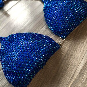 May include: A blue and silver bikini top with crystal embellishments. The top is made of a stretchy fabric and has a halter style strap.