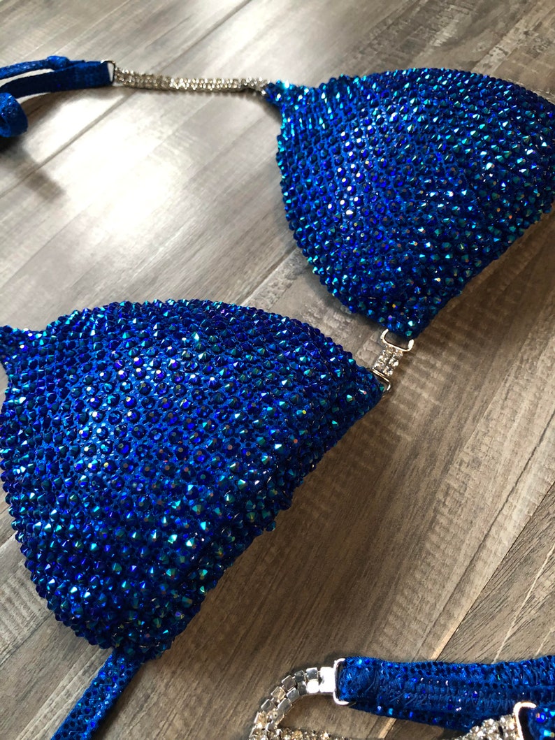 May include: A blue and silver bikini top with crystal embellishments. The top is made of a stretchy fabric and has a halter style strap.