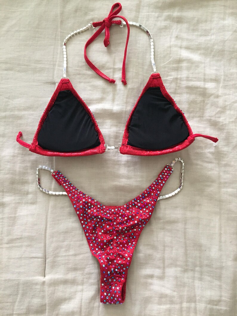 May include: Red and black bikini with crystal embellishments. The top has a halter style with a black lining. The bottom is a high-cut style with a full back.