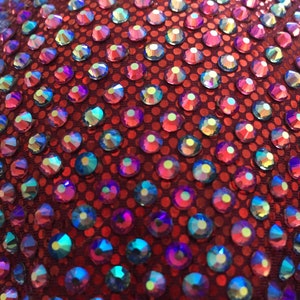 May include: Close-up of a red fabric covered with iridescent blue and purple rhinestones.