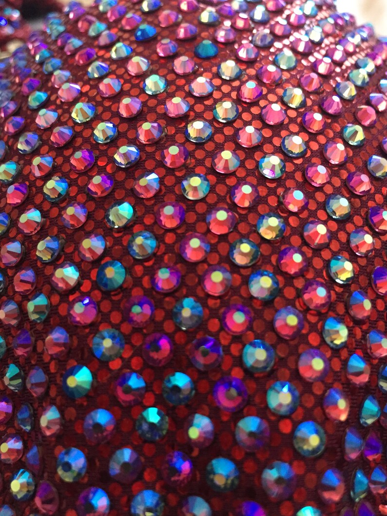 May include: Close-up of a red fabric covered with iridescent blue and purple rhinestones.