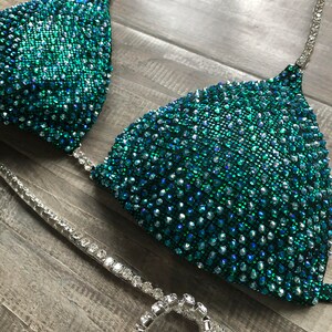 May include: A teal and silver sequined bikini top with a halter strap and a matching bottom. The bikini is decorated with rhinestones.