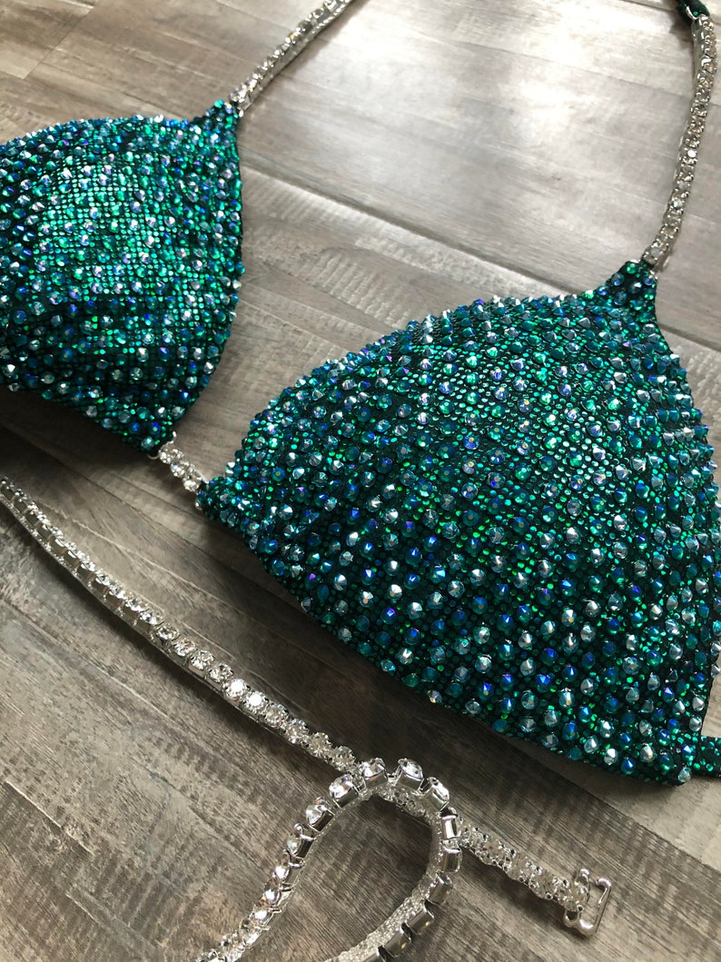 May include: A teal and silver sequined bikini top with a halter strap and a matching bottom. The bikini is decorated with rhinestones.