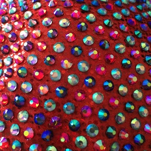 May include: Red fabric covered in iridescent rhinestones. The rhinestones are various shades of blue, green, and red.