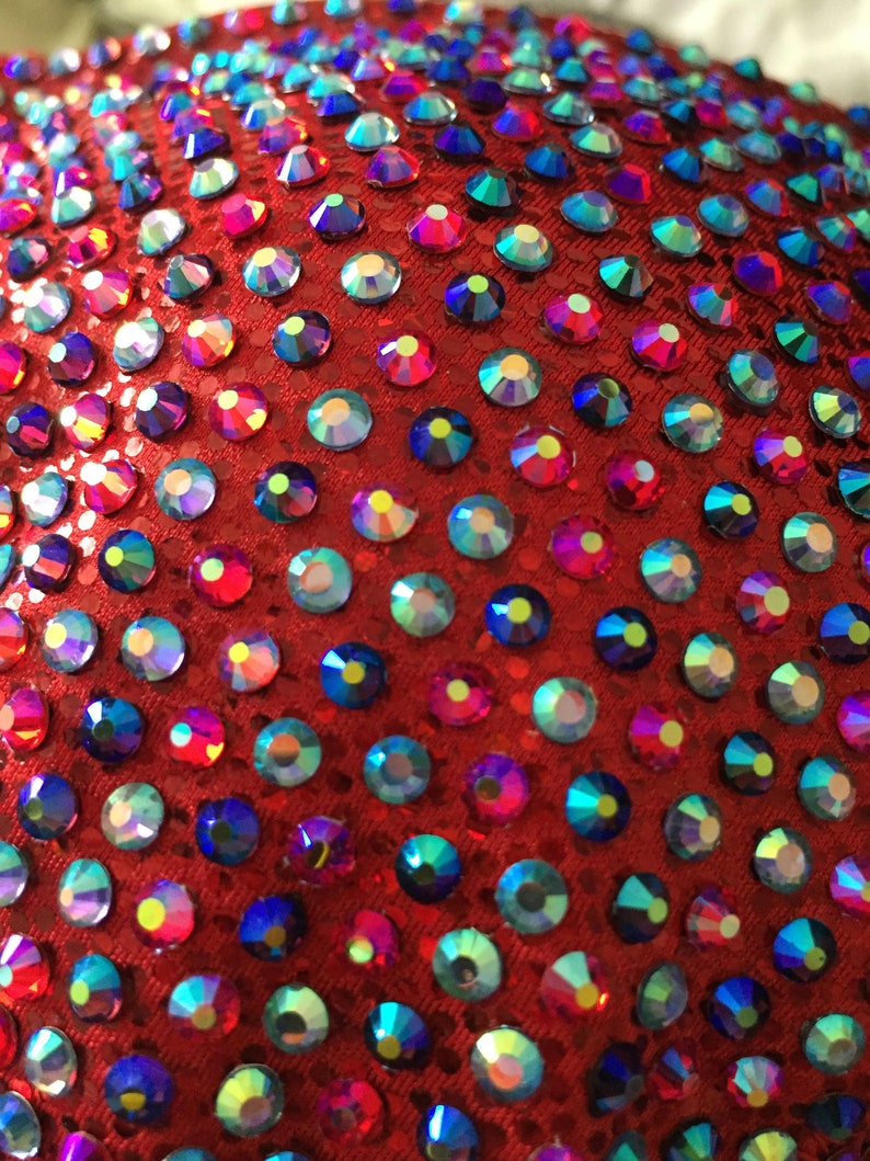 May include: Red fabric covered in iridescent rhinestones. The rhinestones are various shades of blue, green, and red.