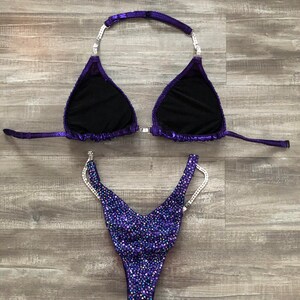 Puede incluir: Parte superior e inferior de bikini de lentejuelas moradas y plateadas. La parte superior tiene un estilo halter con un cierre en la espalda. La parte inferior tiene un corte alto y est&aacute; adornada con pedrer&iacute;a.