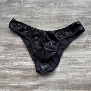 May include: Black underwear with a shiny, silky appearance. The garment has a low-rise waist and a contoured pouch. The fabric has a slight sheen, and the edges are neatly finished with a thin hem.