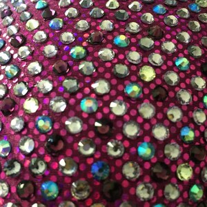Pu&ograve; includere: Primo piano di un tessuto magenta ricoperto da una variet&agrave; di strass iridescenti.
