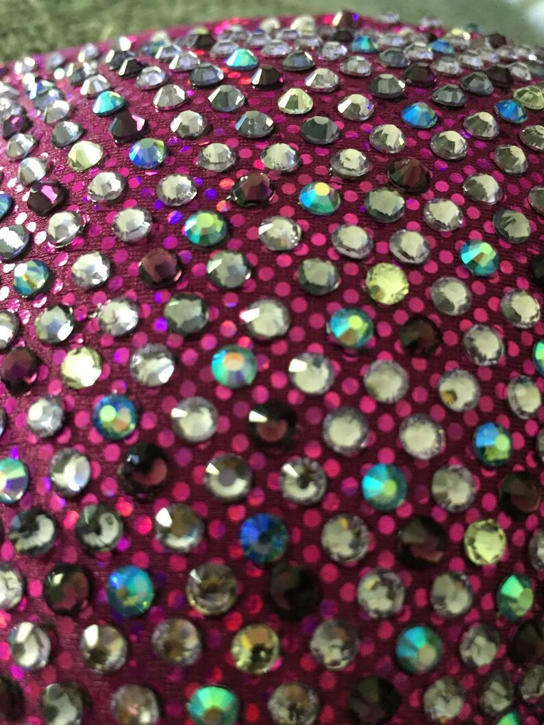 Pu&ograve; includere: Primo piano di un tessuto magenta ricoperto da una variet&agrave; di strass iridescenti.