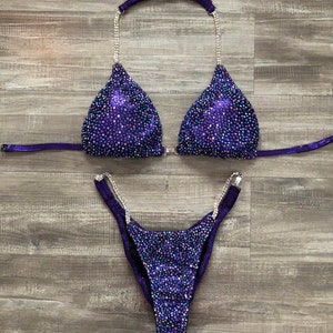 Puede incluir: Traje de competici&oacute;n de bikini con lentejuelas moradas y plateadas con un top halter y una parte inferior de corte alto.