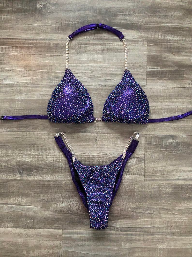 Puede incluir: Traje de competici&oacute;n de bikini con lentejuelas moradas y plateadas con un top halter y una parte inferior de corte alto.
