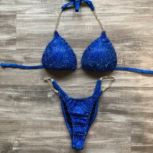 May include: A blue bikini with crystal embellishments. The top has a halter style and the bottom is a cheeky cut.