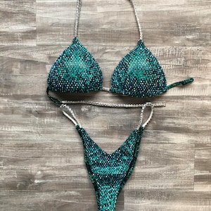 May include: A teal and green sequined bikini with silver straps. The bikini top is a triangle style and the bottom is a cheeky cut.