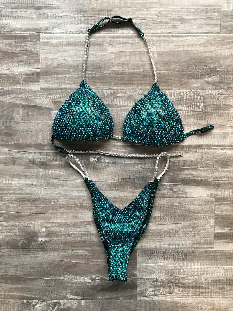 May include: A teal and green sequined bikini with silver straps. The bikini top is a triangle style and the bottom is a cheeky cut.