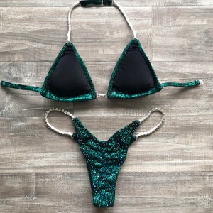 May include: A green and black sparkly bikini with rhinestones. The top is a triangle style with a halter strap and the bottom is a cheeky style.