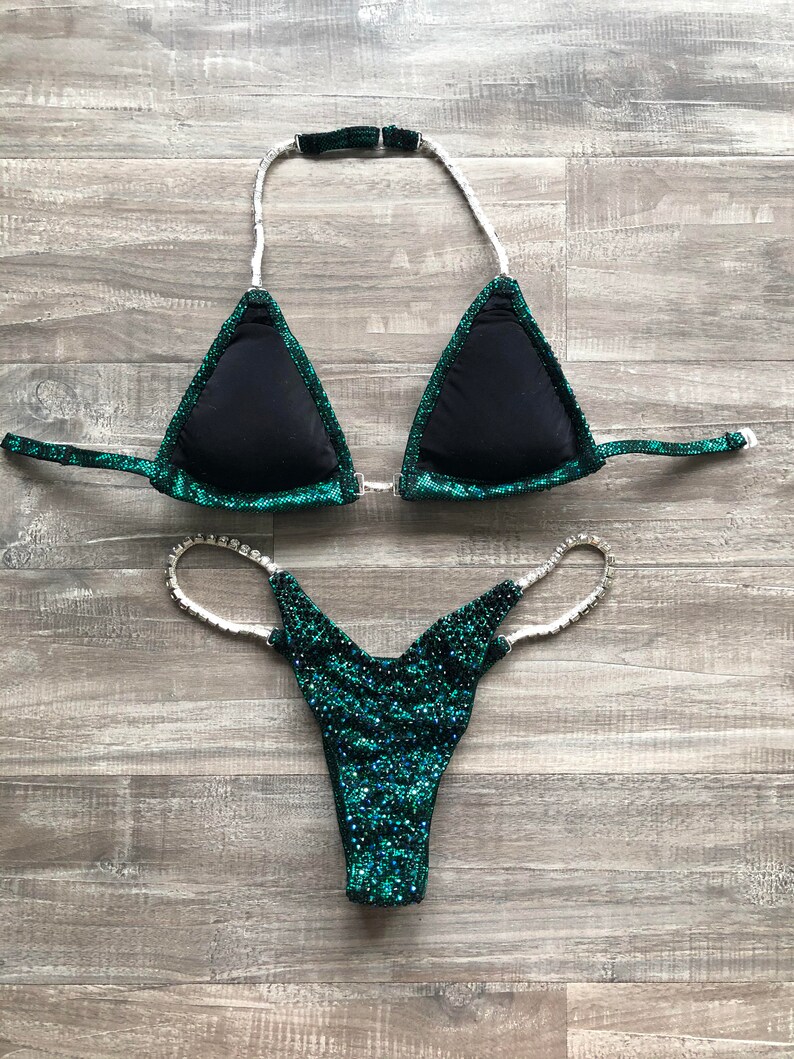 May include: A green and black sparkly bikini with rhinestones. The top is a triangle style with a halter strap and the bottom is a cheeky style.