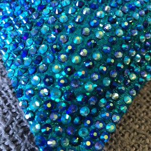 May include: Close-up of a teal fabric covered with iridescent blue rhinestones.