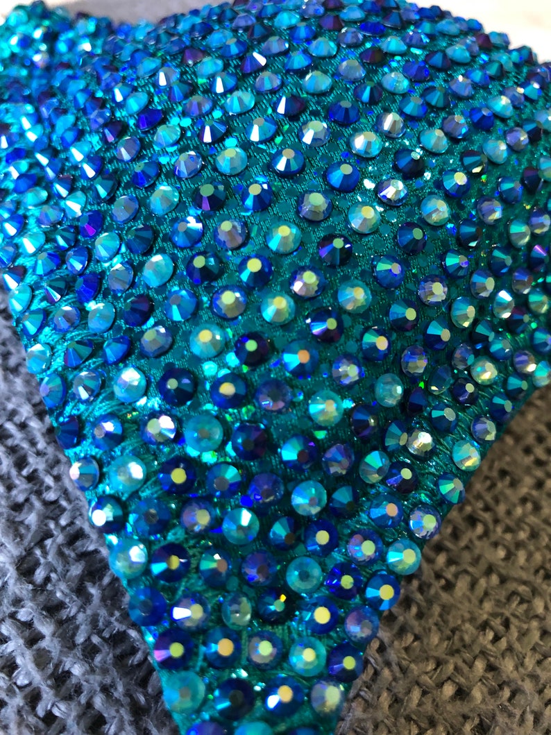 May include: Close-up of a teal fabric covered with iridescent blue rhinestones.