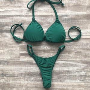 Peut inclure: Un ensemble de bikini vert foncé avec un haut triangle et un bas taille haute. Le bikini a des bretelles et des liens réglables.