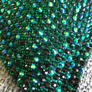 May include: Close-up of a dark green fabric covered in small, sparkling, emerald green rhinestones.