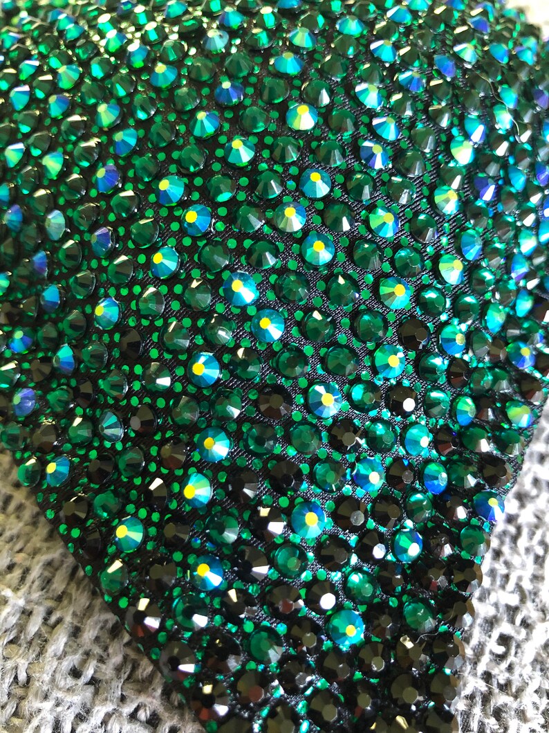 May include: Close-up of a dark green fabric covered in small, sparkling, emerald green rhinestones.