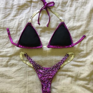 Pu&ograve; includere: Un bikini viola e argento con strass. La parte superiore &egrave; di stile triangolare con fodera nera. La parte inferiore &egrave; di stile a taglio alto con un sottile cinturino su ogni lato.