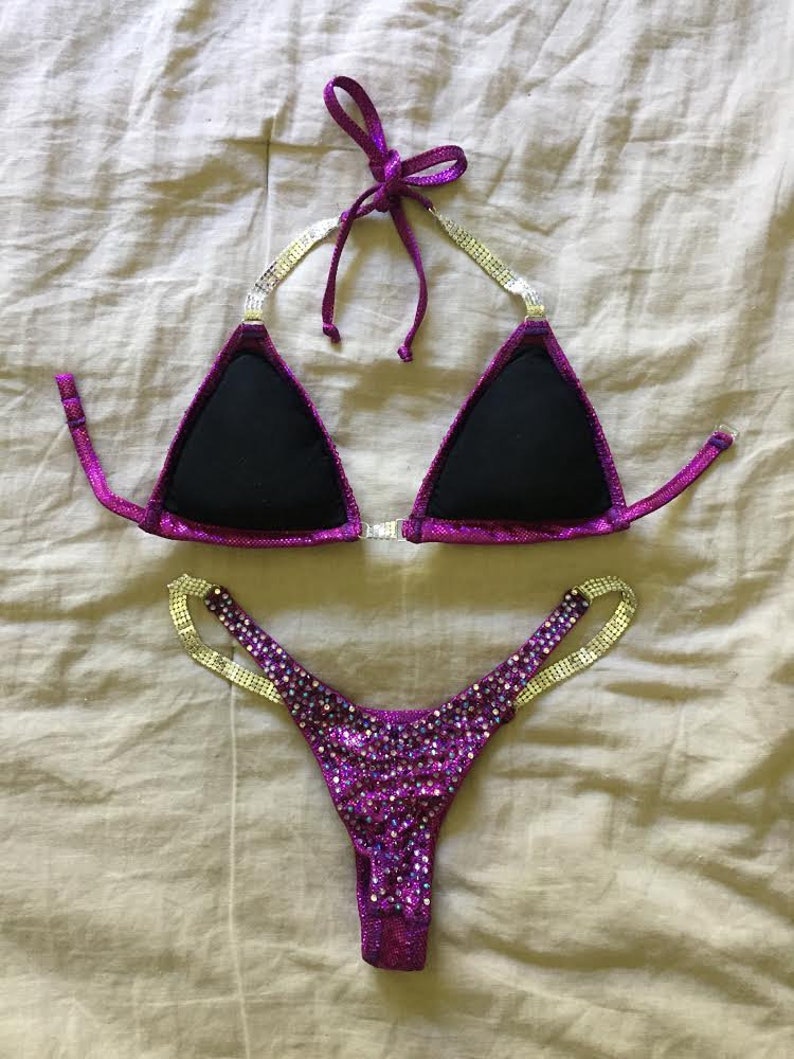 Pu&ograve; includere: Un bikini viola e argento con strass. La parte superiore &egrave; di stile triangolare con fodera nera. La parte inferiore &egrave; di stile a taglio alto con un sottile cinturino su ogni lato.