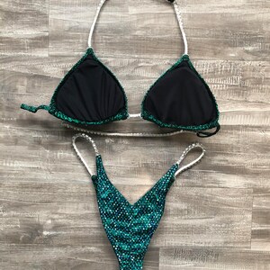 May include: A green and black two-piece swimsuit with rhinestones. The top is a triangle style with a halter strap. The bottom is a high-cut style with a V-shaped front.