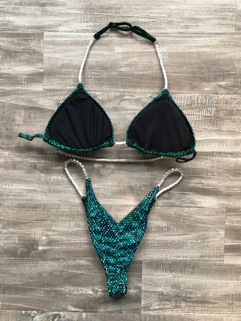 May include: A green and black two-piece swimsuit with rhinestones. The top is a triangle style with a halter strap. The bottom is a high-cut style with a V-shaped front.