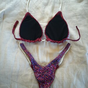 May include: A red and iridescent bikini with crystal embellishments. The top has a halter style with a white strap. The bottom is a high-cut style with a white strap on each side.