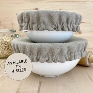 Peut inclure: Deux couvercles de bol en lin gris sur des bols blancs. Le texte "AVAILABLE IN 4 SIZES" est sur un cercle beige.