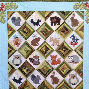 May include: A quilt with a blue and green border features a variety of woodland animals, including owls, squirrels, deer, raccoons, and foxes. The animals are arranged in a diamond pattern on a white background.