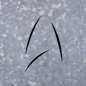May include: A black stylized triangle shape drawn on a silver metallic surface.