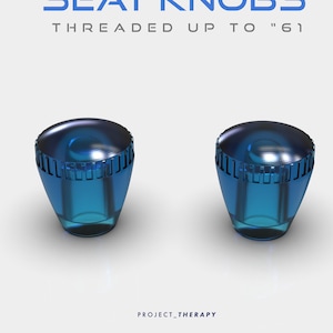 Könnte beinhalten: Zwei blaue Sitzknöpfe mit transparentem Design. Die Knöpfe haben eine abgerundete Oberseite und einen Gewindesockel. Der Text "SEAT KNOBS THREADED UP TO '61" ist über den Knöpfen zu sehen. Der Markenname "PROJECT_THERAPY" steht unten.