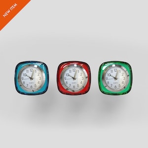 May include: Three square quartz clocks with white faces and black numerals. The clocks have blue, red, and green frames. The clocks show the time as 10:09. The words "QUARTZ" are printed on the clock faces. The upper left corner has a "NEW ITEM" sticker.