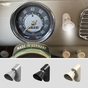 Puede incluir: Un pequeño foco LED ajustable montado en el salpicadero de un coche clásico junto a un velocímetro. La luz está disponible en acabados plateado, negro y crema, con una cabeza cónica, una base cilíndrica y un icono de encendido en el lateral.