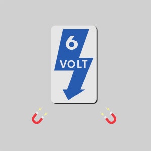 以下が含まれることがあります： 青い稲妻の形に白い文字で「6 VOLT」と書かれた長方形の看板。 赤い蹄鉄型の磁石が2つあり、それぞれ黄色い稲妻が描かれています。すべて灰色の背景に配置されています。