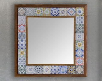 May include: Square mirror with a wooden frame and a border of decorative tiles. The tiles feature a variety of blue, white, yellow, and green patterns. The mirror is mounted on a gray wall.