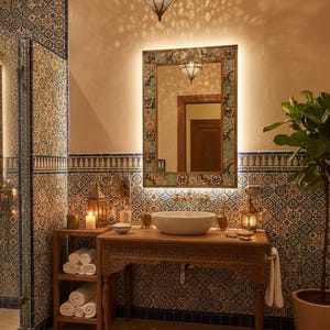 May include: A bathroom with a Moroccan theme, featuring a carved wooden vanity with a white basin, a decorative mirror, and patterned tiles. A hanging lantern and candles add to the ambiance. A potted plant and a patterned rug complete the scene.