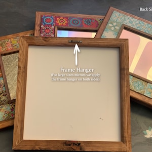 May include: Several decorative mirrors with wooden frames are displayed. The mirrors have colorful tile accents and are in various sizes. The back of one mirror shows a frame hanger. Text on the image reads "Frame Hanger" and "Back Side".