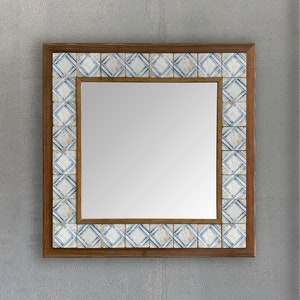 May include: Square mirror with a wooden frame and a border of blue and white patterned tiles. The mirror has a reflective surface and is designed for wall mounting. The frame is a warm brown color, and the tiles have a geometric design.