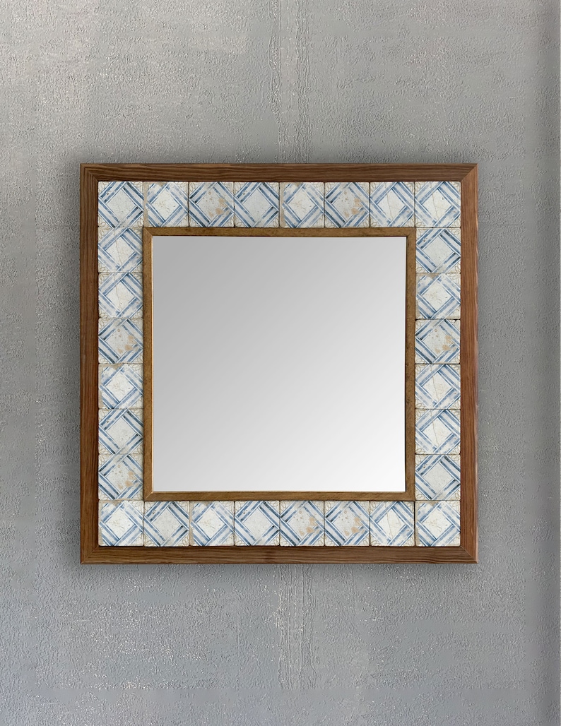May include: Square mirror with a wooden frame and a border of blue and white patterned tiles. The mirror has a reflective surface and is designed for wall mounting. The frame is a warm brown color, and the tiles have a geometric design.