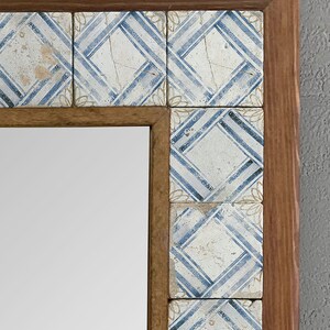 May include: A rectangular mirror with a wooden frame. The frame is decorated with square tiles featuring a blue and white geometric pattern. The mirror is a decorative item.